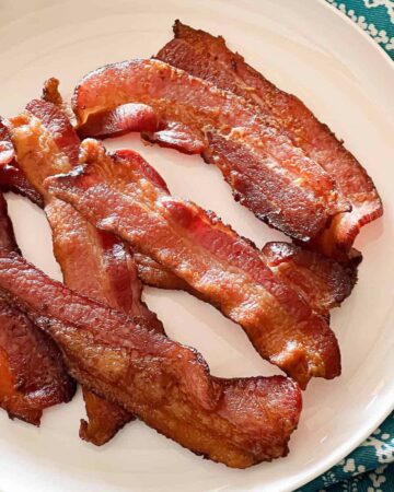 Crispy strips of bacon on a white plate on top of a teal patterned towel.