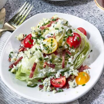 Classic wedge salad on a white plate with a gold fork in the background.