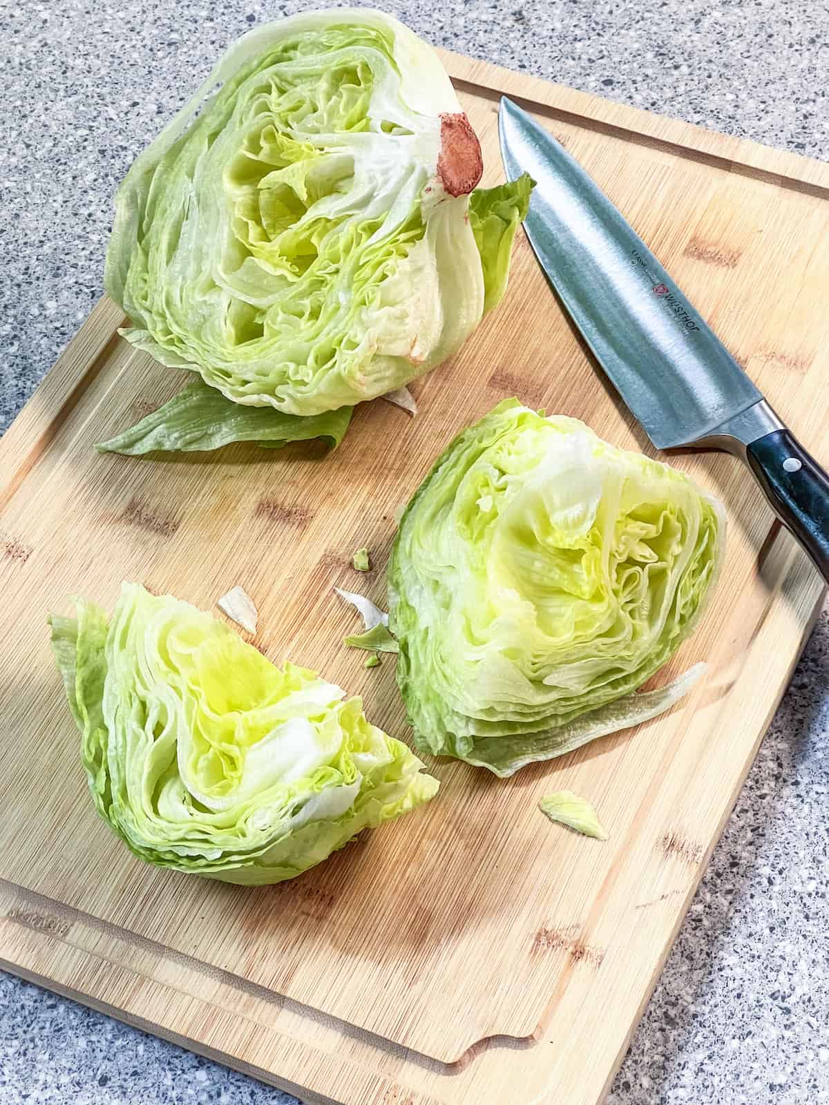 Head of iceberg lettuce cut in half and quarters on a cutting board with a knife.