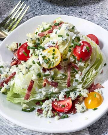 Classic wedge salad on a white plate with a gold fork in the background.