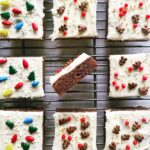 Gingerbread cookie bars with cream cheese frosting and holiday sprinkles on a baking rack.