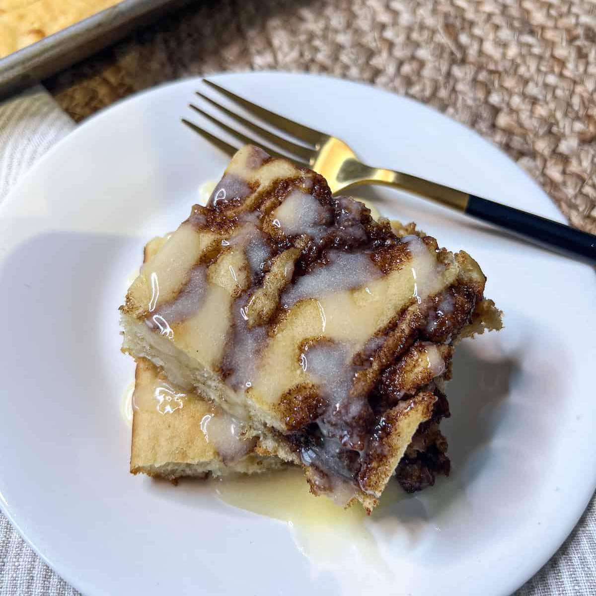 Square slices of cinnamon roll pancakes on a white plate with a gold fork.