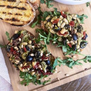 Cannellini bean salad and arugula on top of grilled bread slices on a wood cutting board.