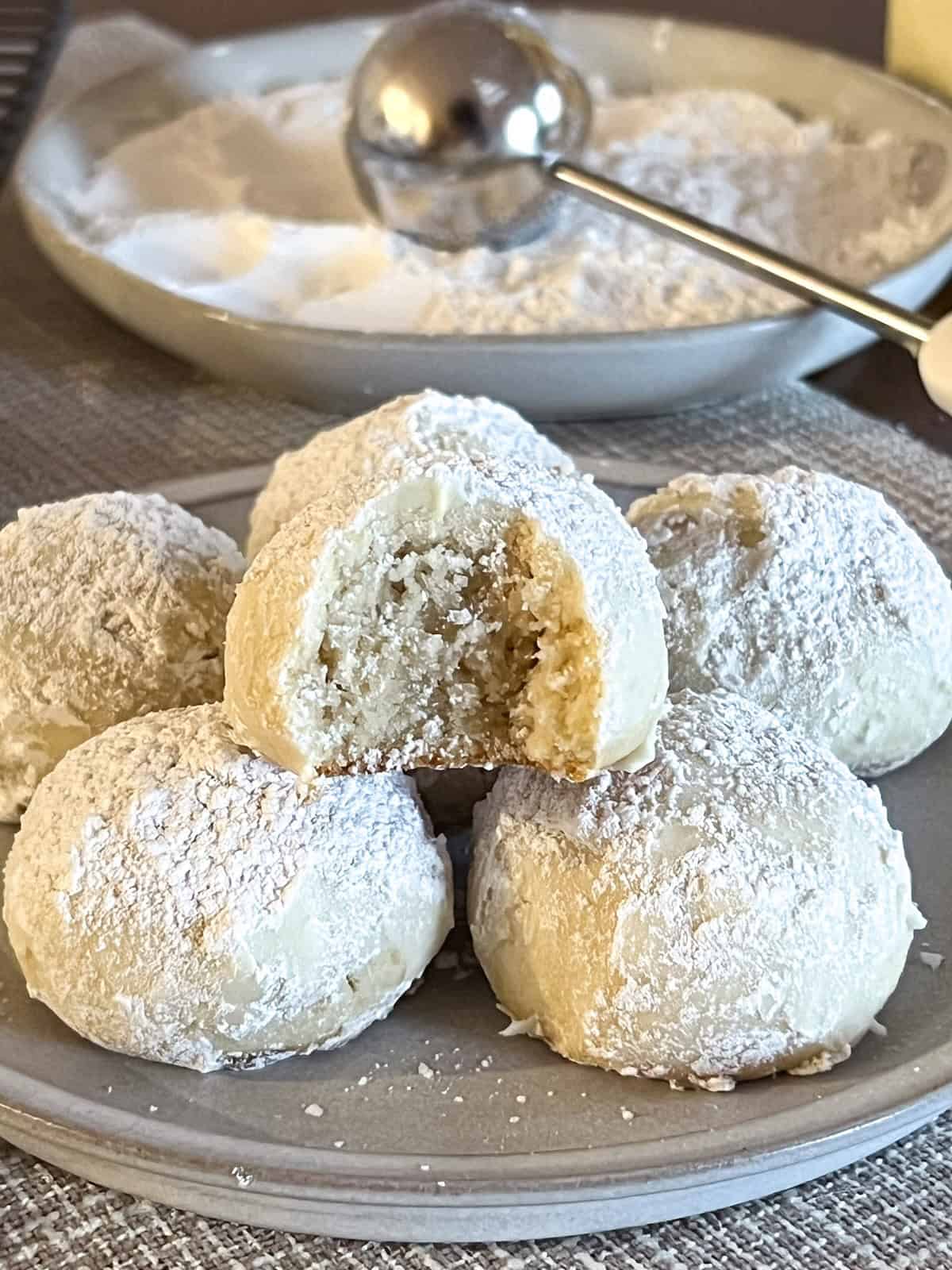 Snowball cookie. with a bite taken out of it on top of more cookies on a plate.