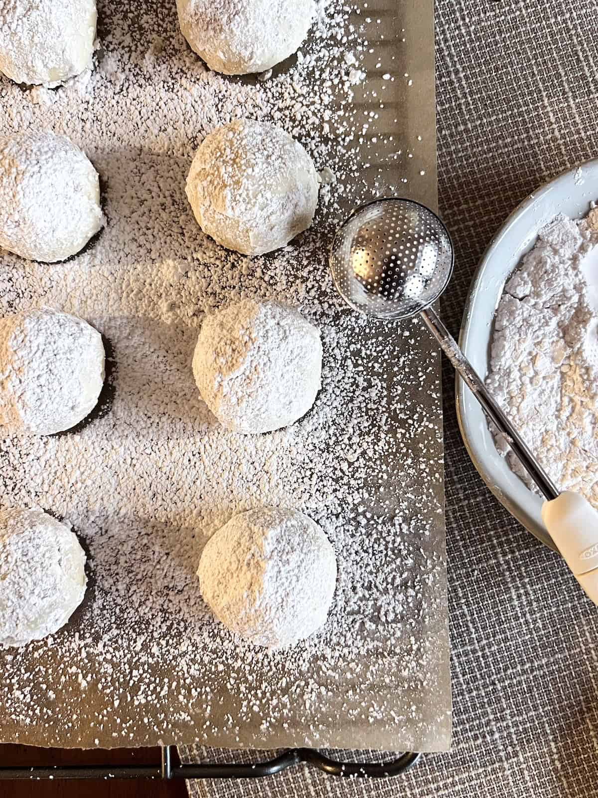 Snowball cookies on parchment paper with a bakers dusting wand and powdered sugar