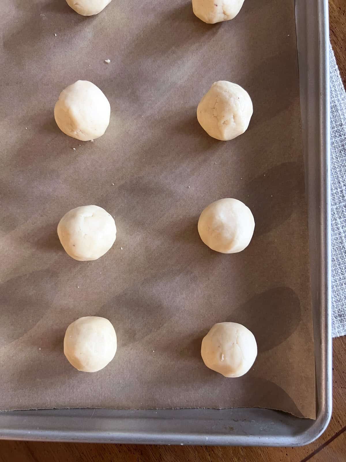 Cookie dough balls on a parchment paper lined baking sheet.