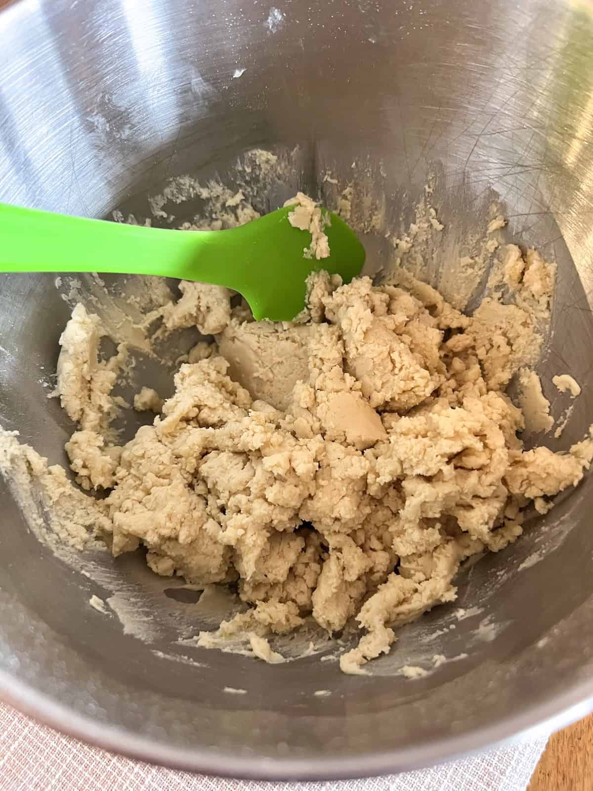 Cookie dough in the bowl of a stand mixer with a green silicone spatula.