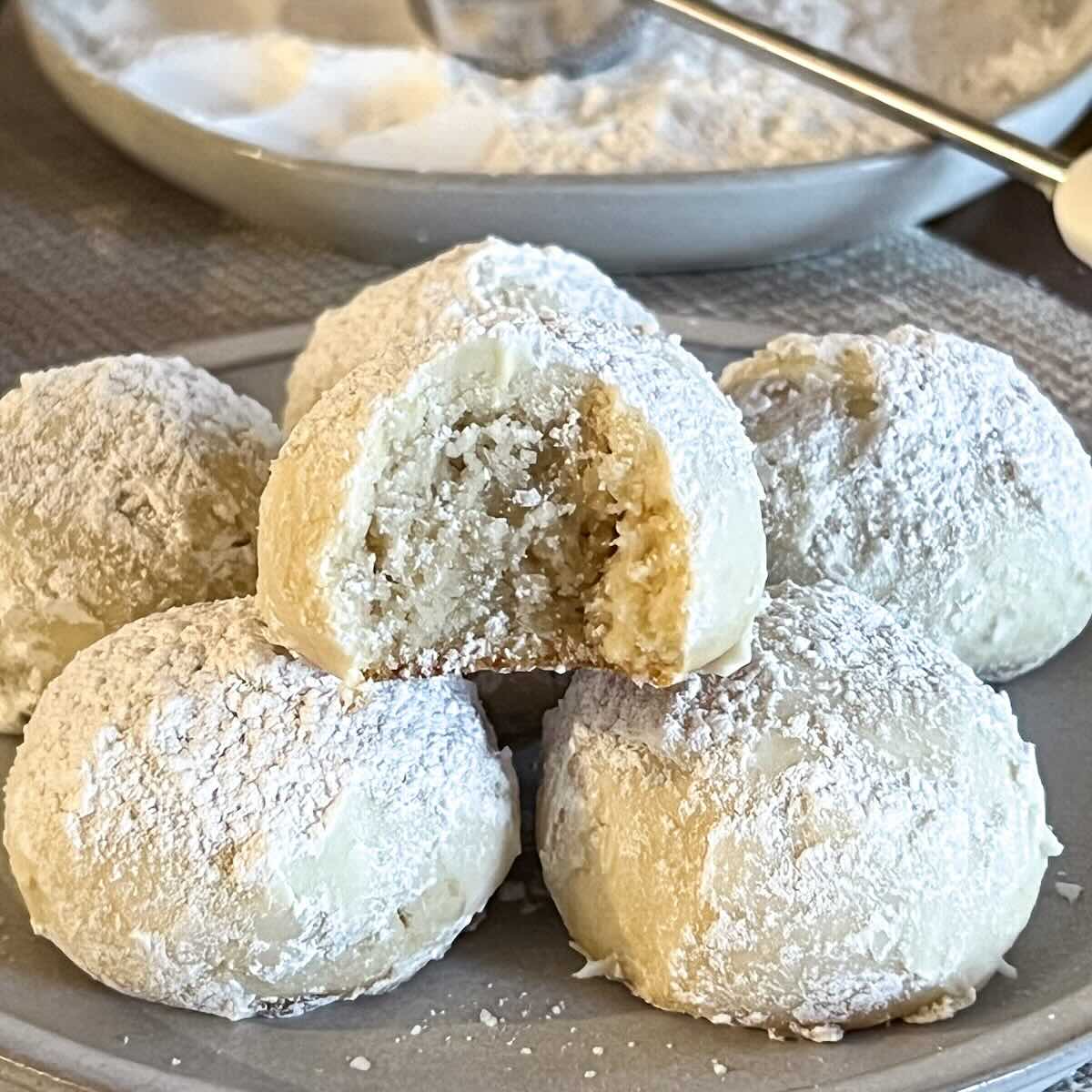 Snowball cookie. with a bite taken out of it on top of more cookies on a plate.