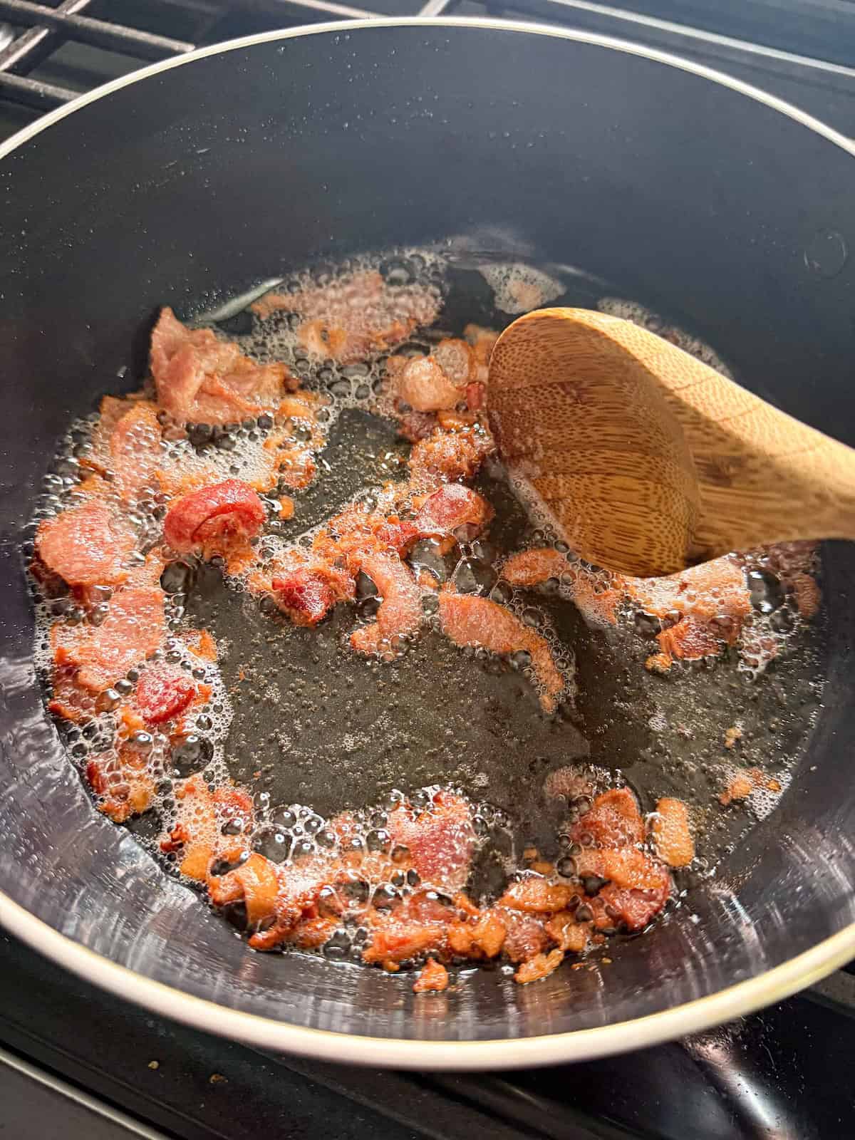 Crispy bacon pieces in a frying pan with a wooden spoon.