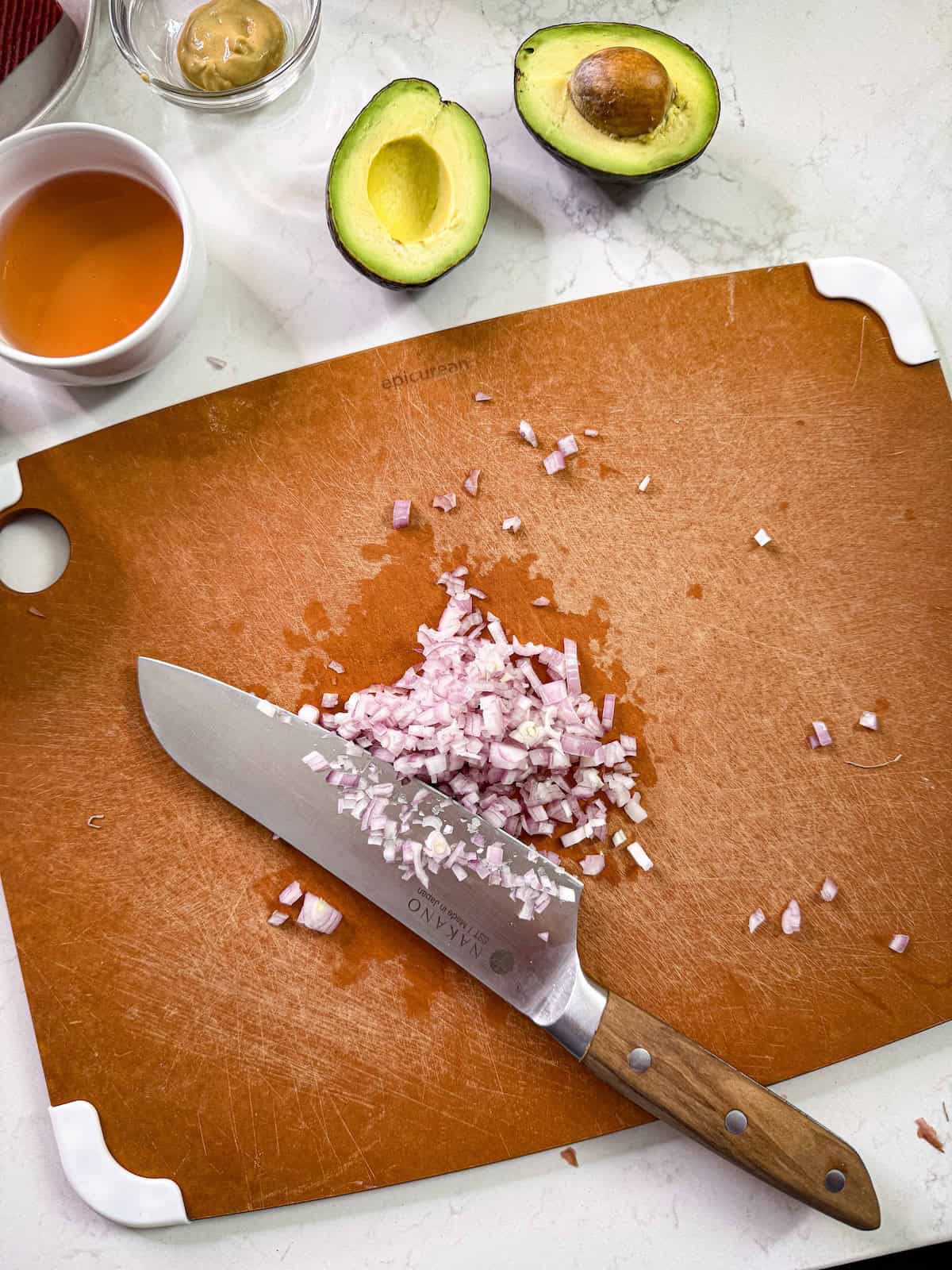 Minced shallots on a cutting board with a knife.