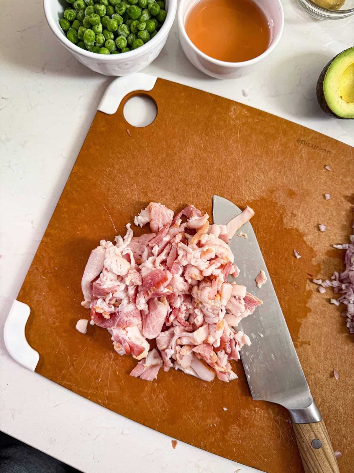 Chopped raw bacon on a cutting board with a knife.