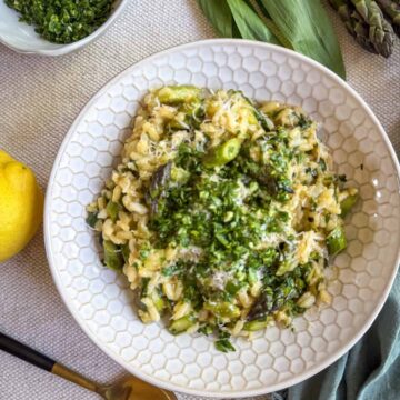Creamy asparagus and ramp risotto topped with gremolata and Parmesan in a white bowl, served with lemon and a gold spoon.