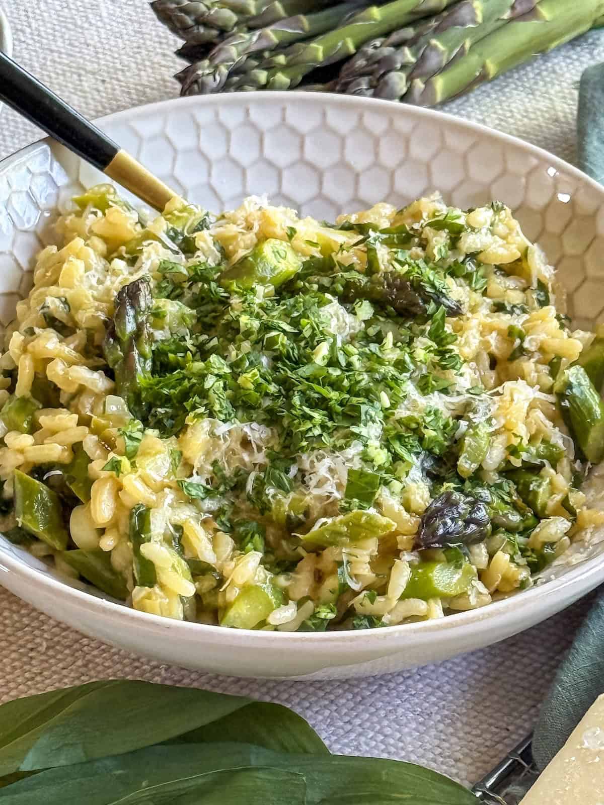 Asaparagus and ramp risotto in a white honeycomb pattern bowl with a gold spoon.