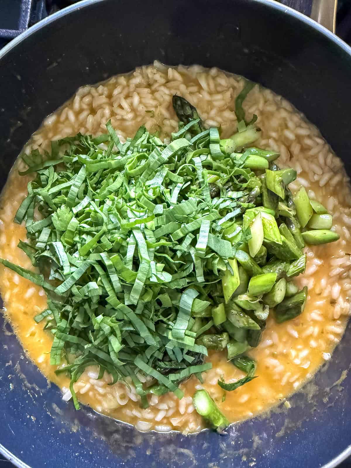 Sauteed asparagus and thinly sliced ramp leaves added to pot of creamy risotto.