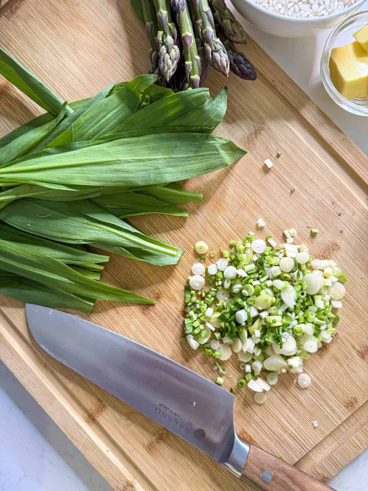 Thinly sliced ramp bulbs on a wood cutting board with whole ramp leaves and a knife.