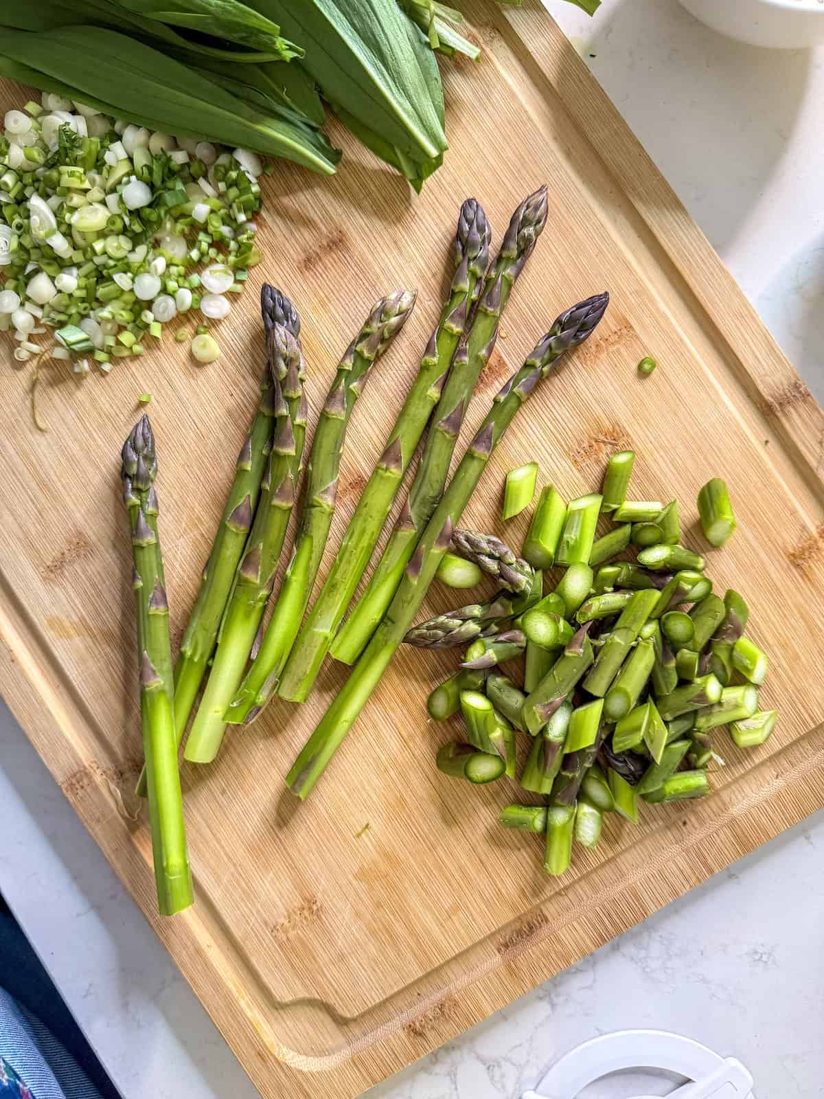 Whole trimmed asparagus spears and some cut into one inch pieces on a wood cutting board.