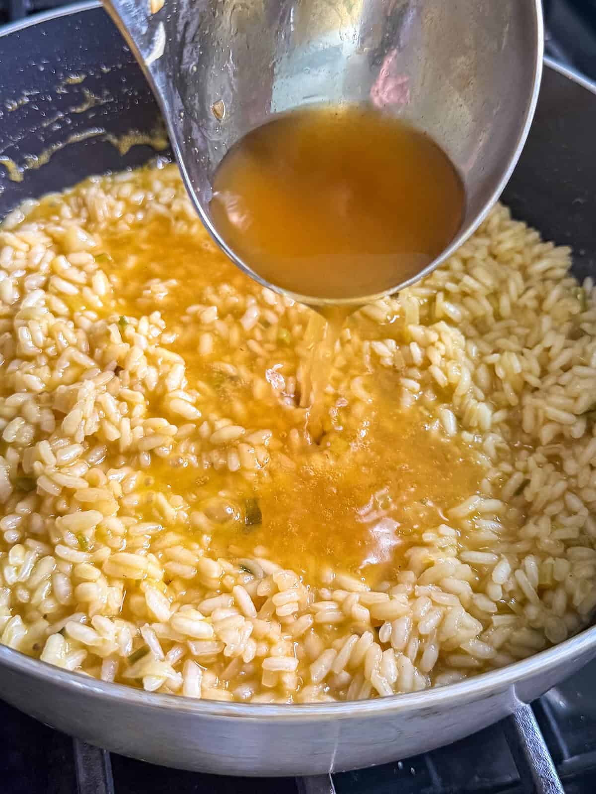 Ladle of hot broth being poured into pan of risotto.