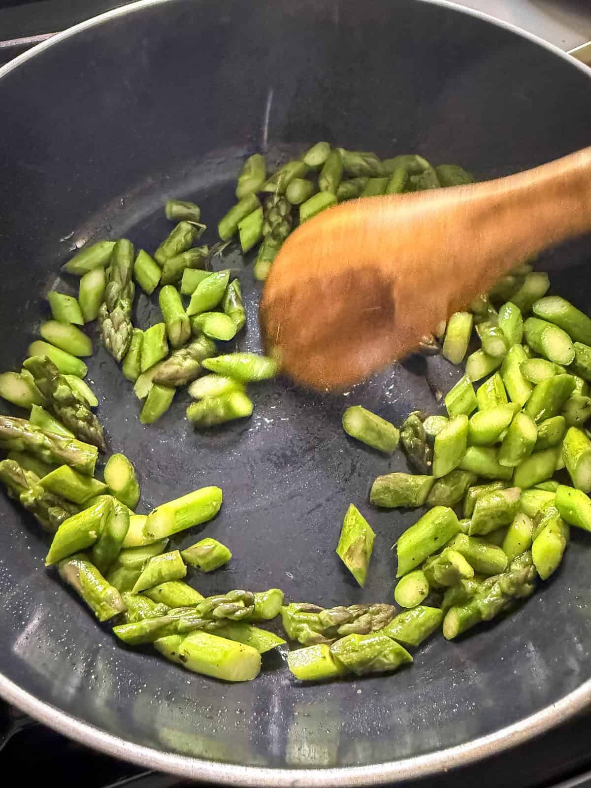 Sautéed asparagus being stirred with a wooden spoon in a pan.