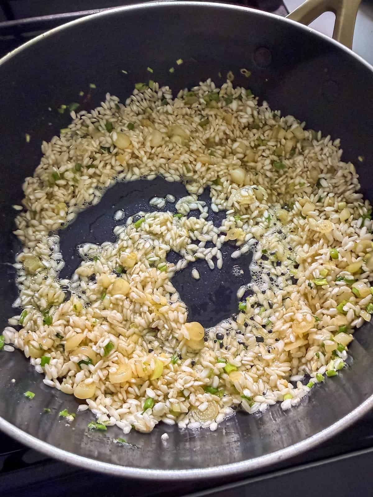 Arborio rice toasting in a pan with sauteed ramps.