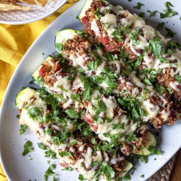 Zucchini halves stuffed with ground beef and rice topped with melted cheese and fresh cilantro on a platter.
