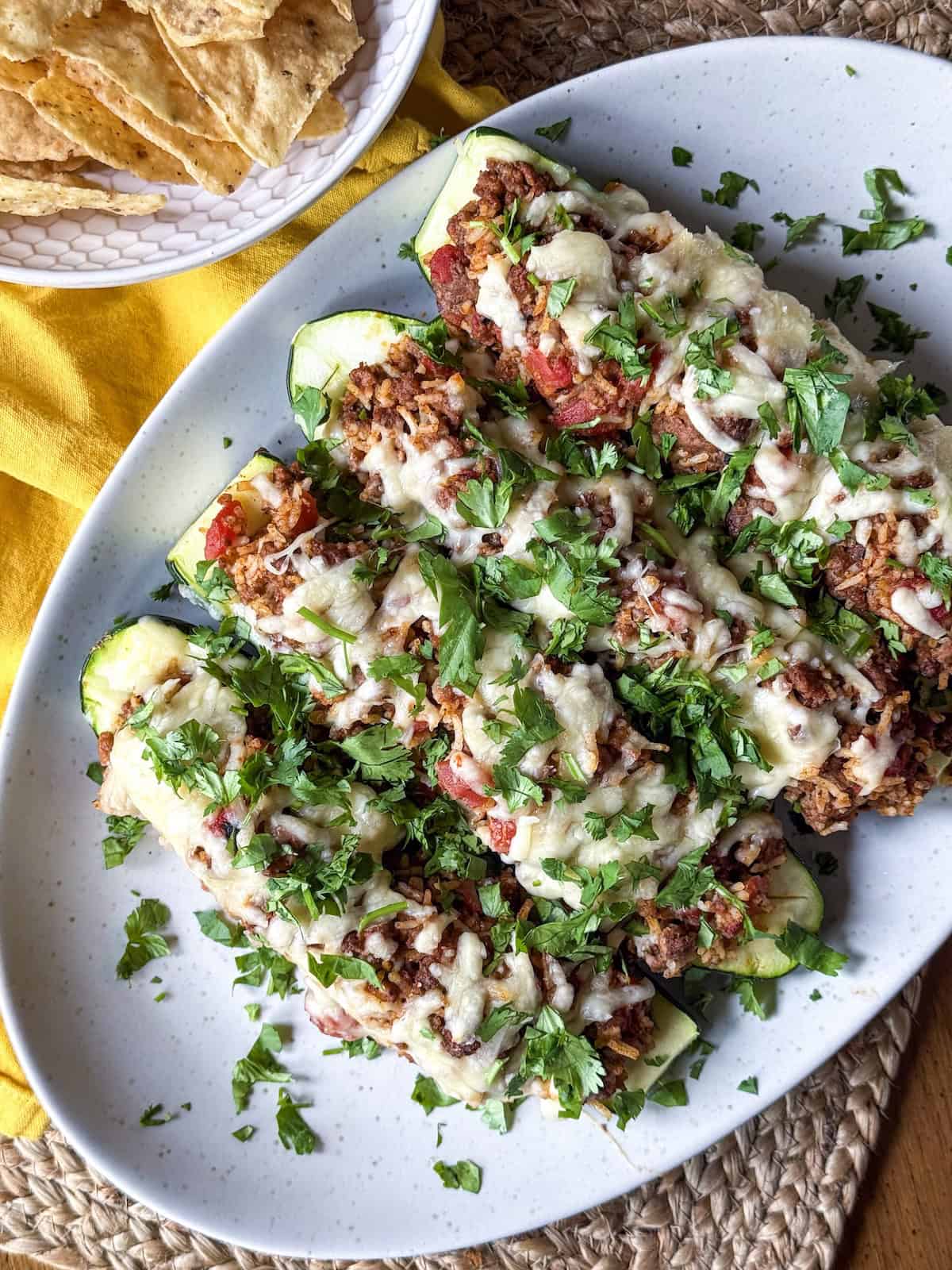 Zucchini halves stuffed with ground beef and rice topped with melted cheese and fresh cilantro on a platter.