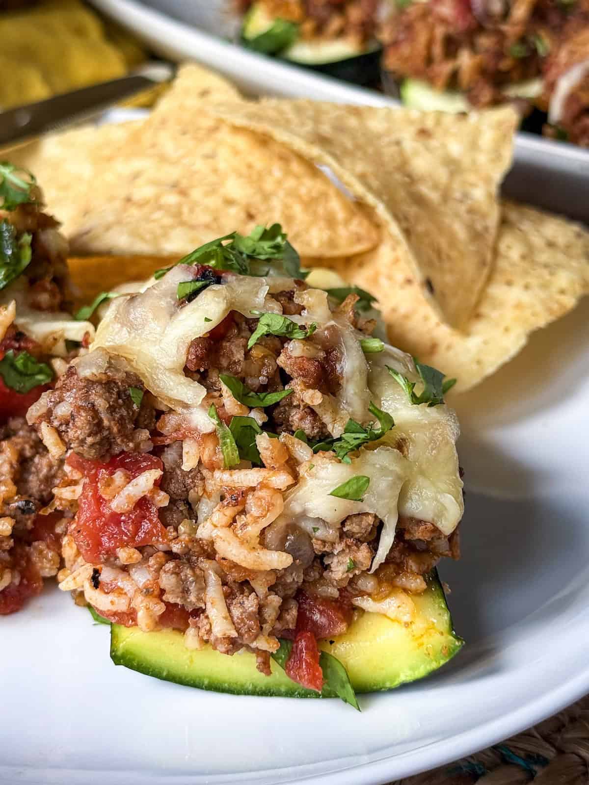 Zucchini boat stuffed with ground beef and rice with tortilla chips on a plate.
