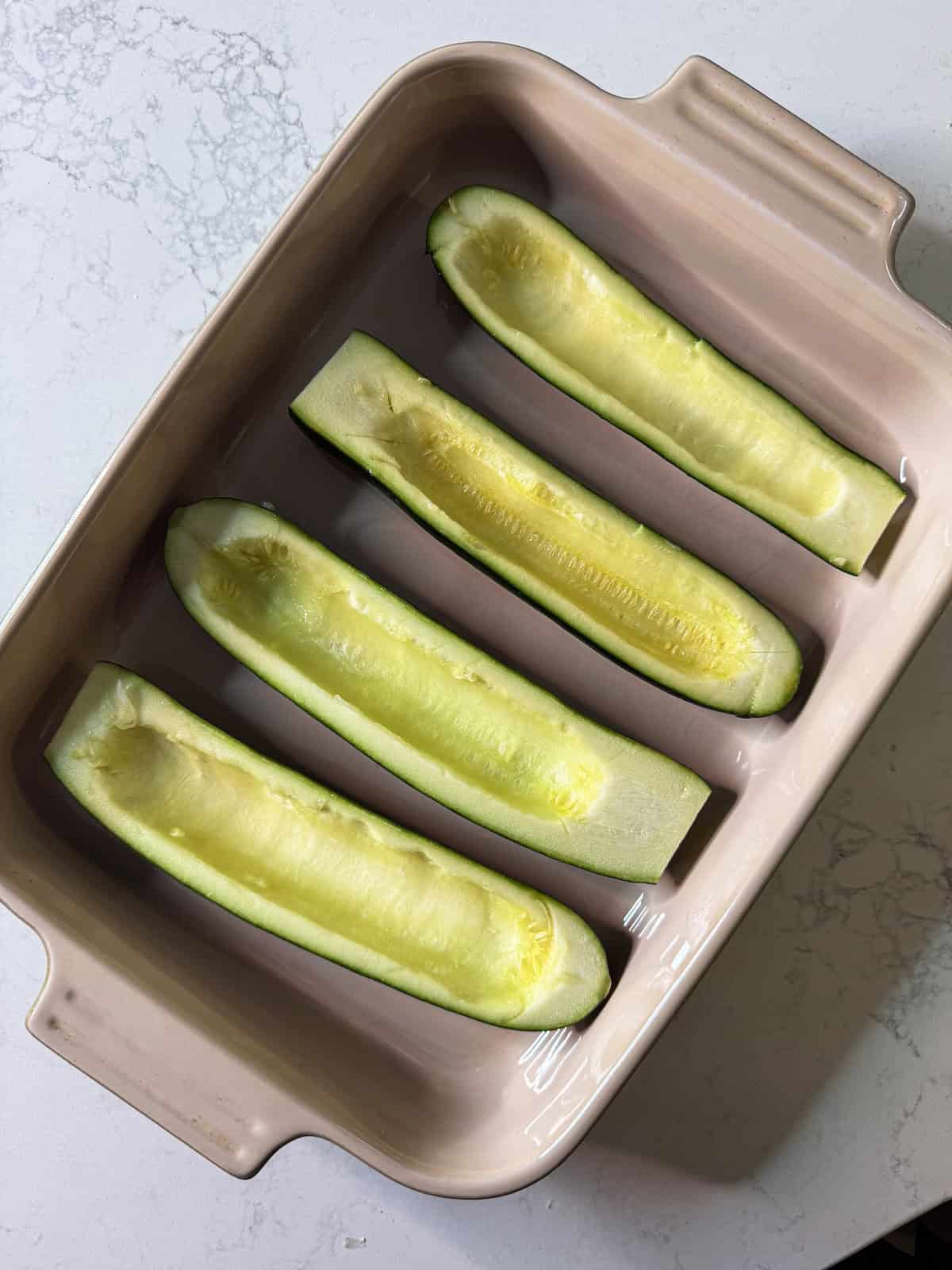 Hollowed out zucchini halves in a baking dish.