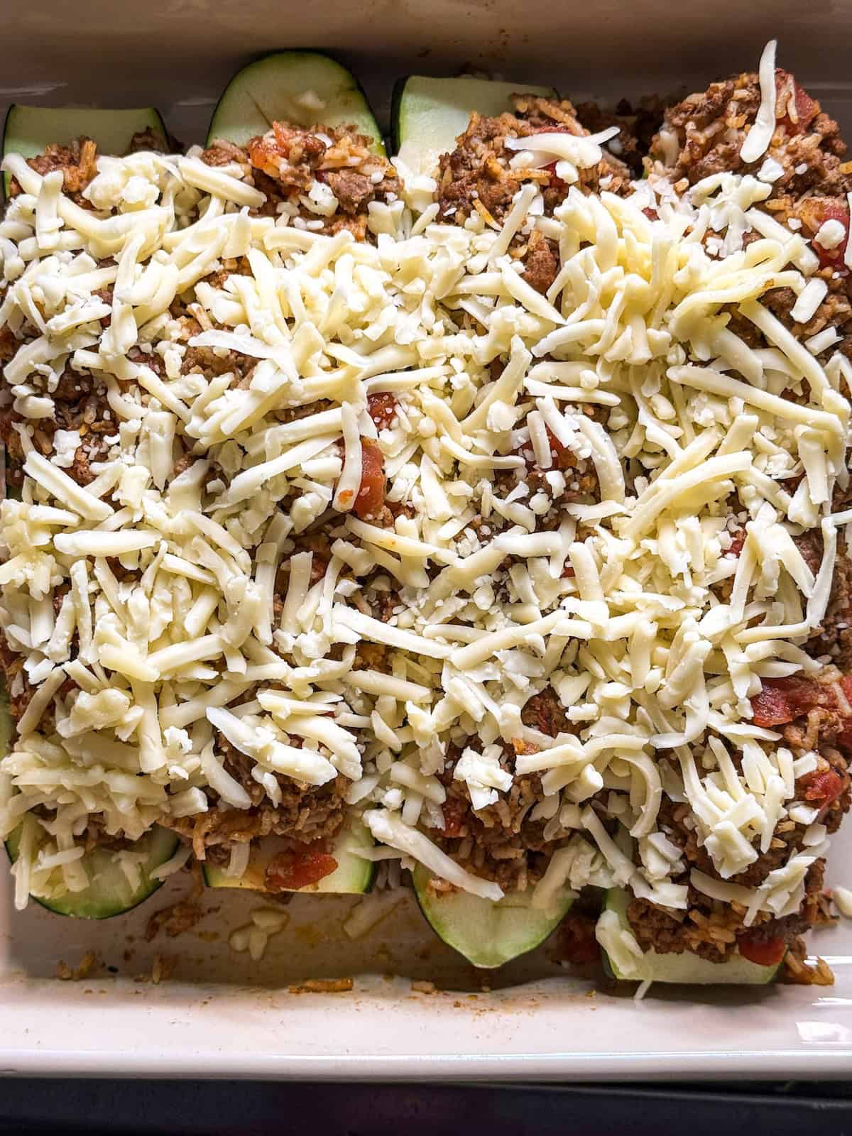 Stuffed zucchini topped with shredded cheese in a baking dish.