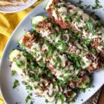 Zucchini halves stuffed with ground beef and rice topped with melted cheese and fresh cilantro on a platter.