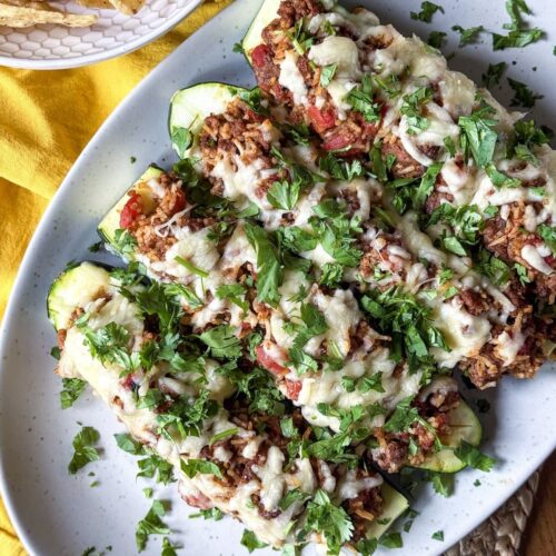 Zucchini halves stuffed with ground beef and rice topped with melted cheese and fresh cilantro on a platter.