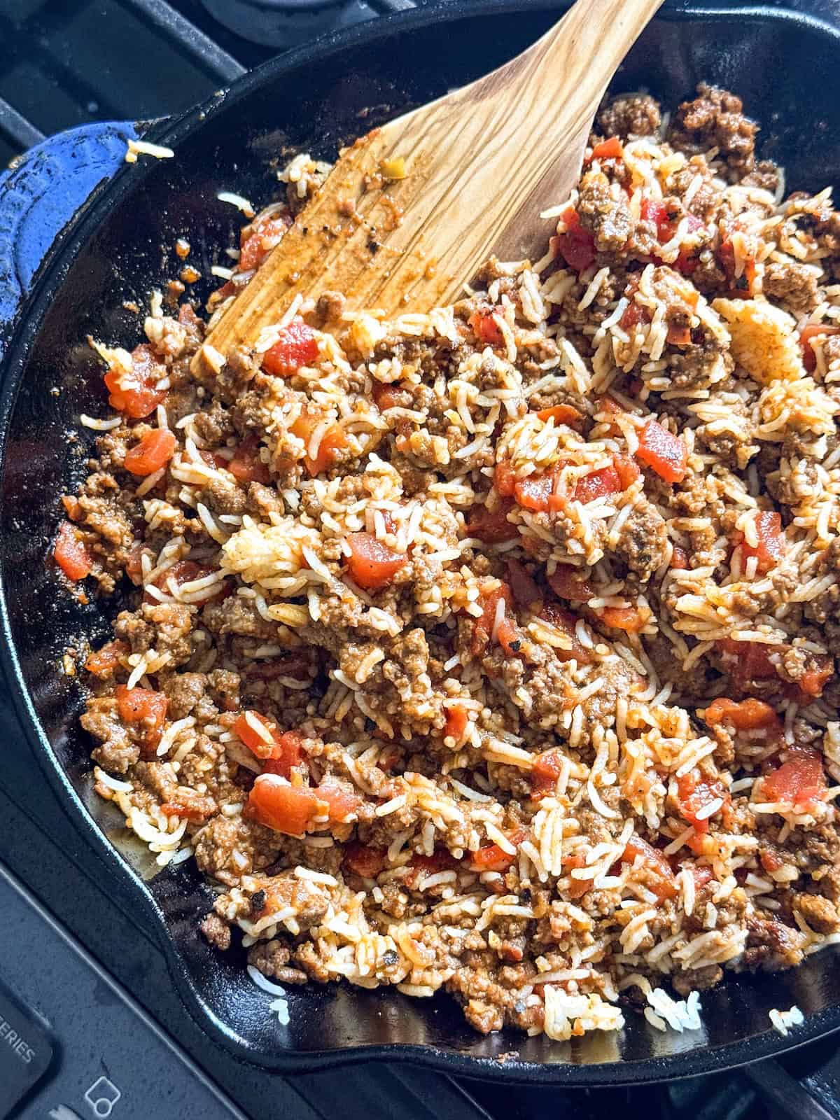 Ground beef and rice filling in a blue cast iron skillet with a wooden spatula.