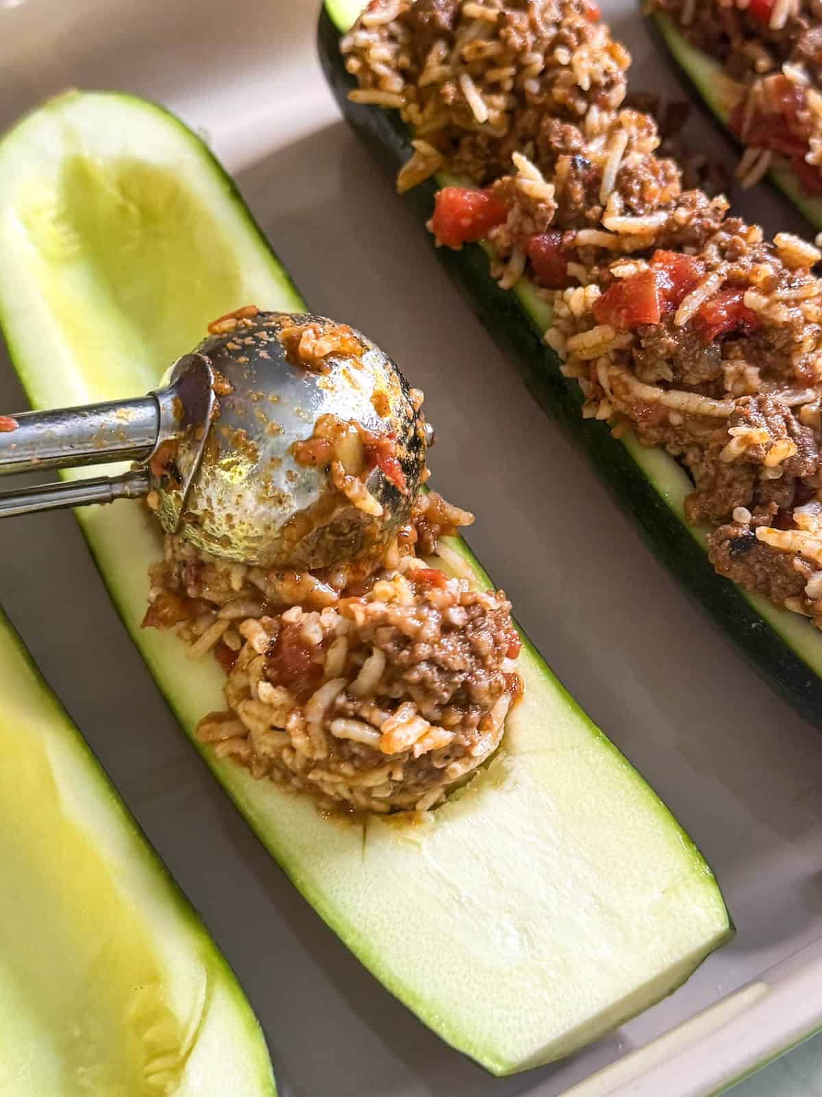Using a cookie scoop to spoon filling into zucchini boats.