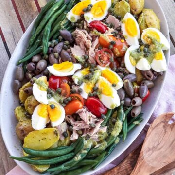 French Nicoise Salad on a platter with wooden serving spoons.