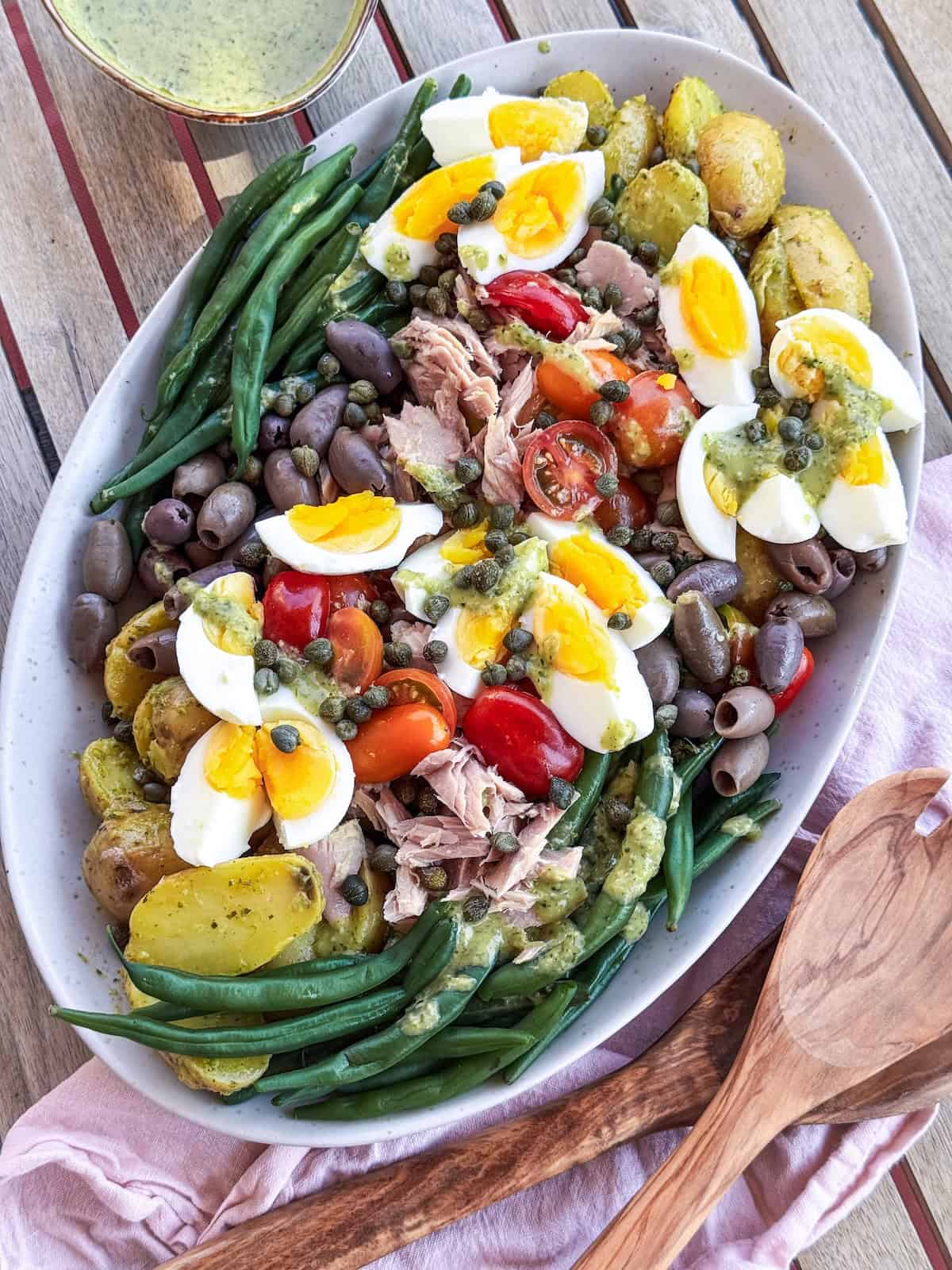 French Nicoise Salad on a platter with wooden serving spoons.