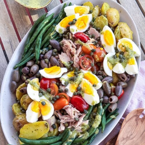 French Nicoise Salad on a platter with wooden serving spoons.