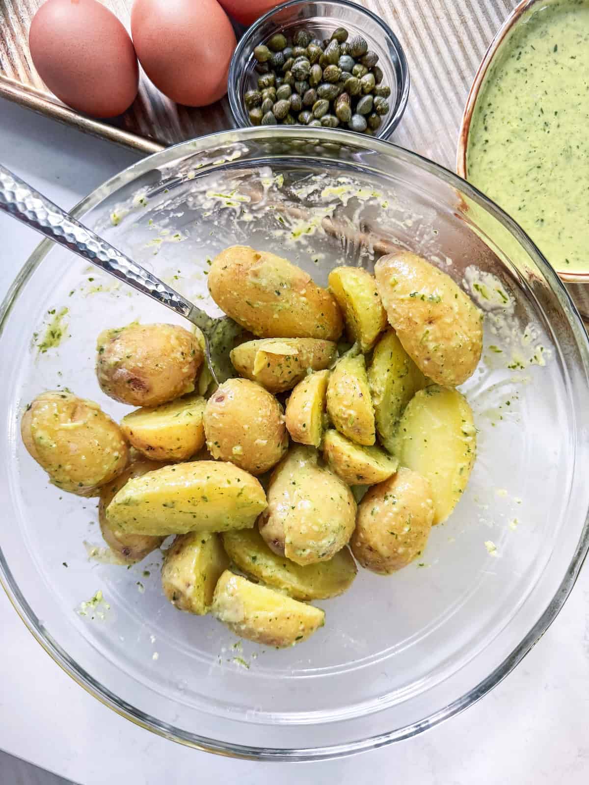 Boiled halved potatoes tossed in dressing in a glass bowl. 