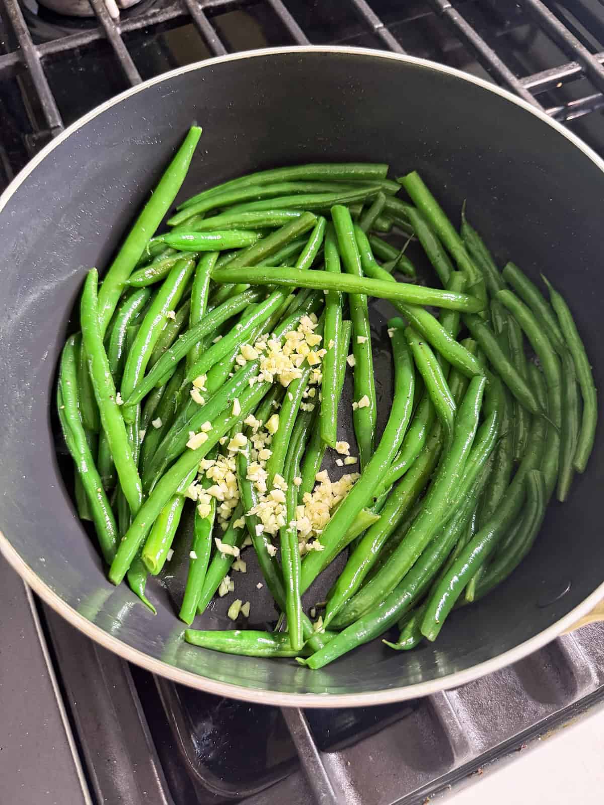 Garlic added to sauteed string beans in a pan.