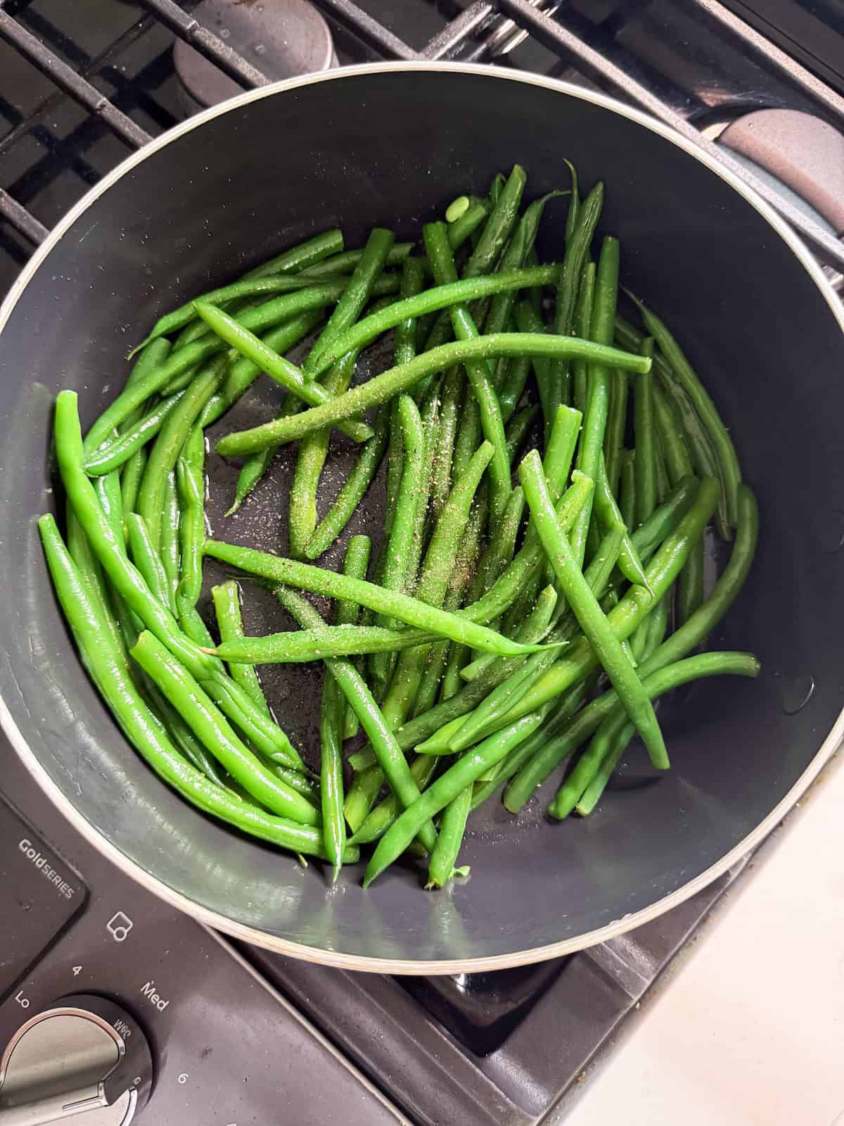 Sauteeing French green beans in a pan with olive oil, salt and pepper.