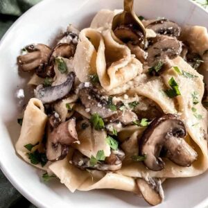 Creamy mushroom pappardelle pasta with garlic parmesan sauce and fresh parsley in a white bowl.