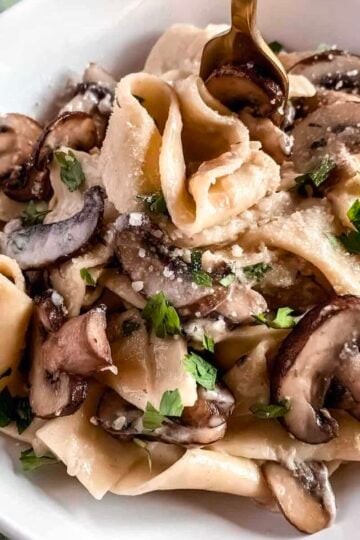 Creamy mushroom pappardelle pasta with garlic parmesan sauce and fresh parsley in a white bowl.