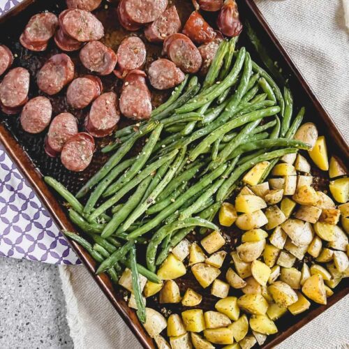 Oven baked sausage, potatoes and green beans on a copper sheet pan.