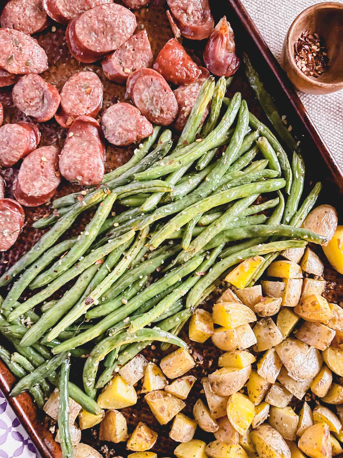 Cooked sausage, potatoes and green beans on a copper sheet pan.